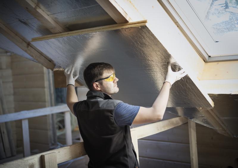 A man in protective eyewear installing insulation in a sunny loft
