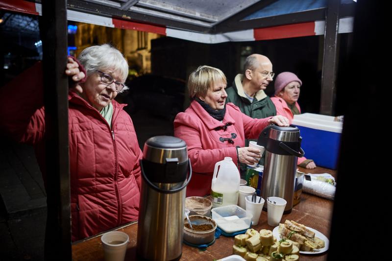 Four volunteers serving food and drink at an outdoor soup kitchen