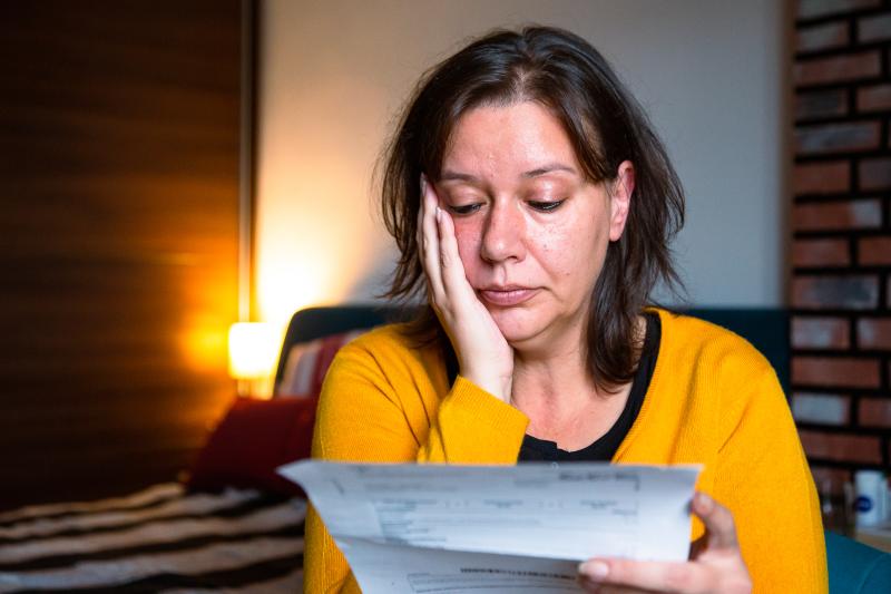 A woman is looking worried as she reads her energy bill