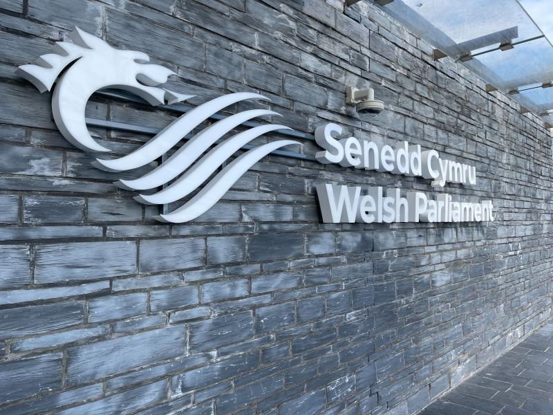 Wall with "Senedd Cymru Welsh Parliament" written on it next to the Welsh parliament's logo