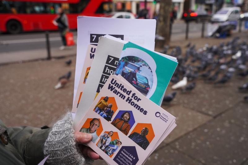 A person's hand holding a selection of United for Warm Homes leaflets