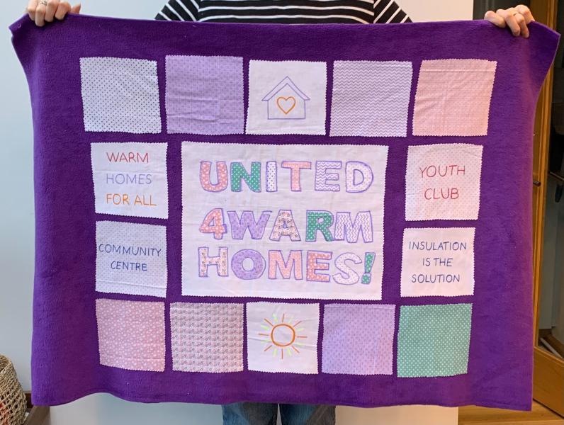 A blanket with square fabric attached showing warm homes messages and images