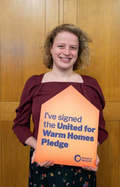 Woman holding an orange pledge sign that says "I've signed the United for Warm Homes pledge"