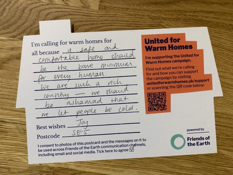 A postcard in the shape of a home with a handwritten message: "I'm calling for warm homes for all because a safe and comfortable home should be the bare minimum for every human. We are such a rich country - we should be ashamed that we let people be cold. Joy."