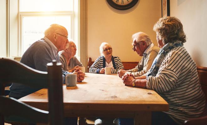A group of older people sitting at a kitchen table drinking tea