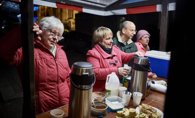 Four volunteers serving food and drink at an outdoor soup kitchen