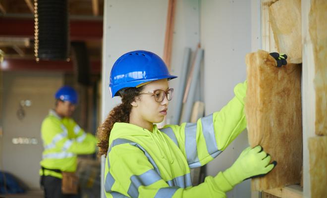 Woman and her colleague in the background installing wall insulation on a building site