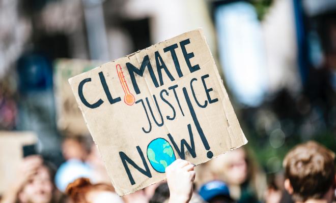 A close up of a hand drawn placard at a protest which reads "climate justice now!"